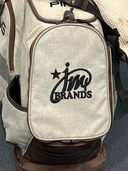 Gray golf bag with the JM4 Brands logo embroidered in black on the pocket