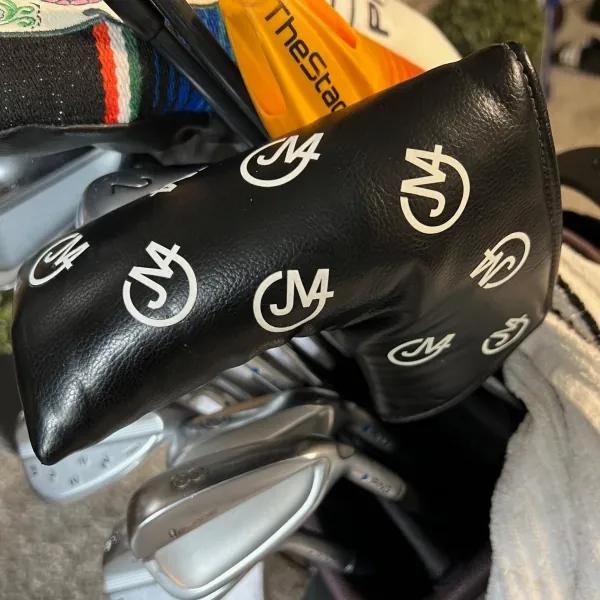 Black golf headcover printed with JM4 logos, in a golf bag