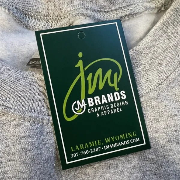 Green JM4 Brands graphic design and apparel hang tag on a gray shirt