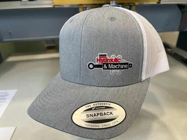 Heather gray and white mesh trucker cap with the Laramie Hydraulic & Machine logo embroidered on the front