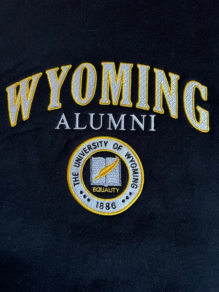 Black crewneck with Wyoming Alumni and the University of Wyoming seal embroidered in white and gold