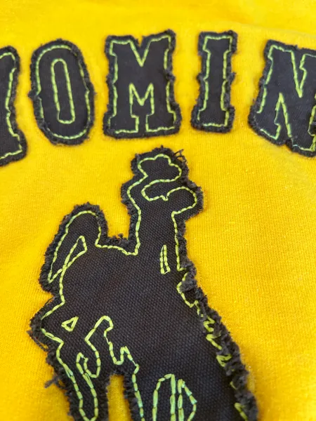 Gold sweatshirt with raw-edge dark appliqué Wyoming letters and a bucking horse, close up